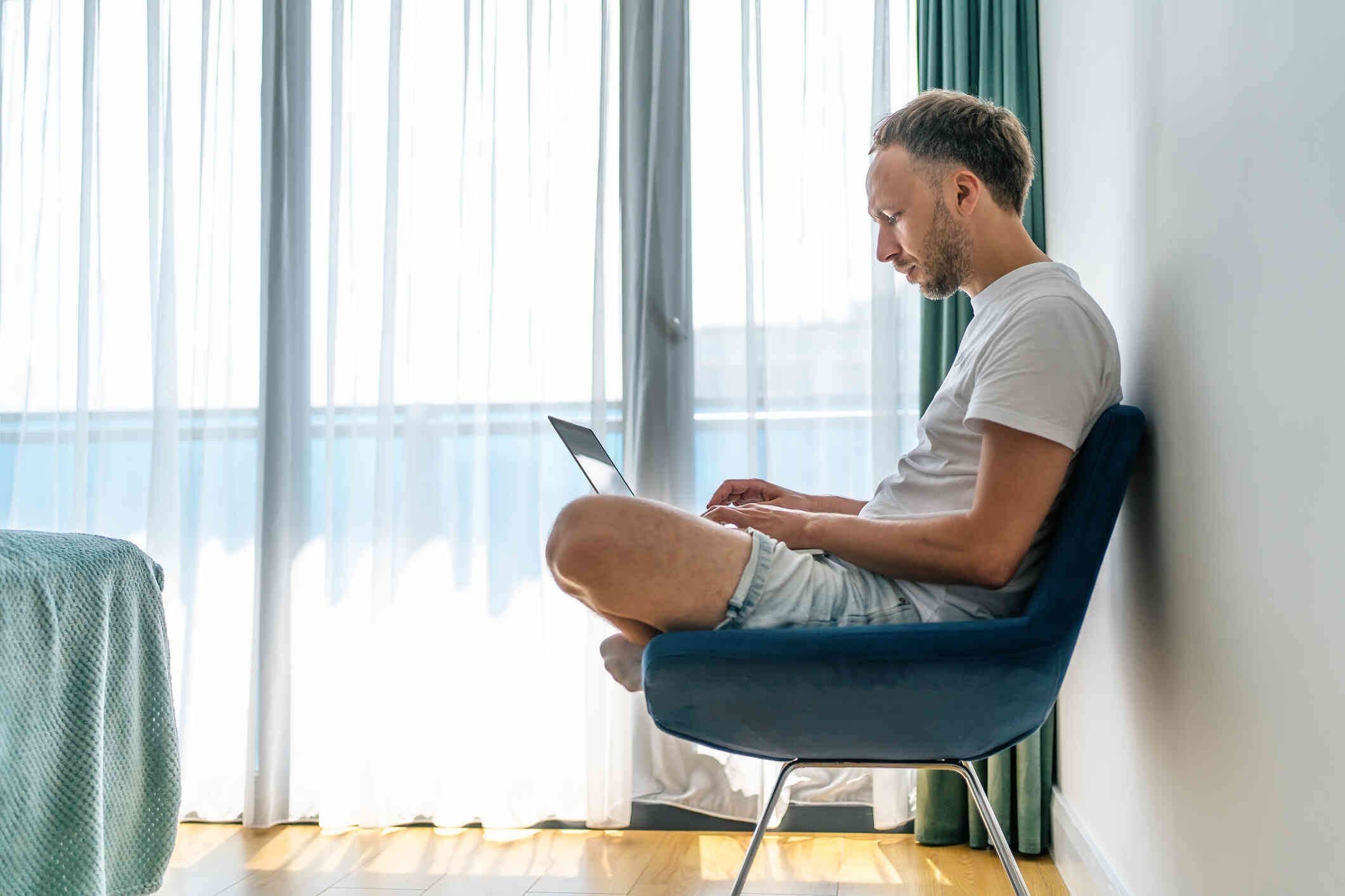 A man seated on a chair, busy typing on his laptop.